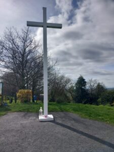 Croix blanche dans parc sous ciel nuageux.
