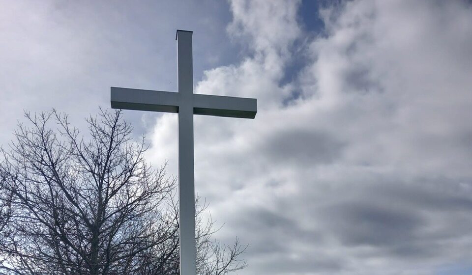 Croix blanche dans parc sous ciel nuageux.